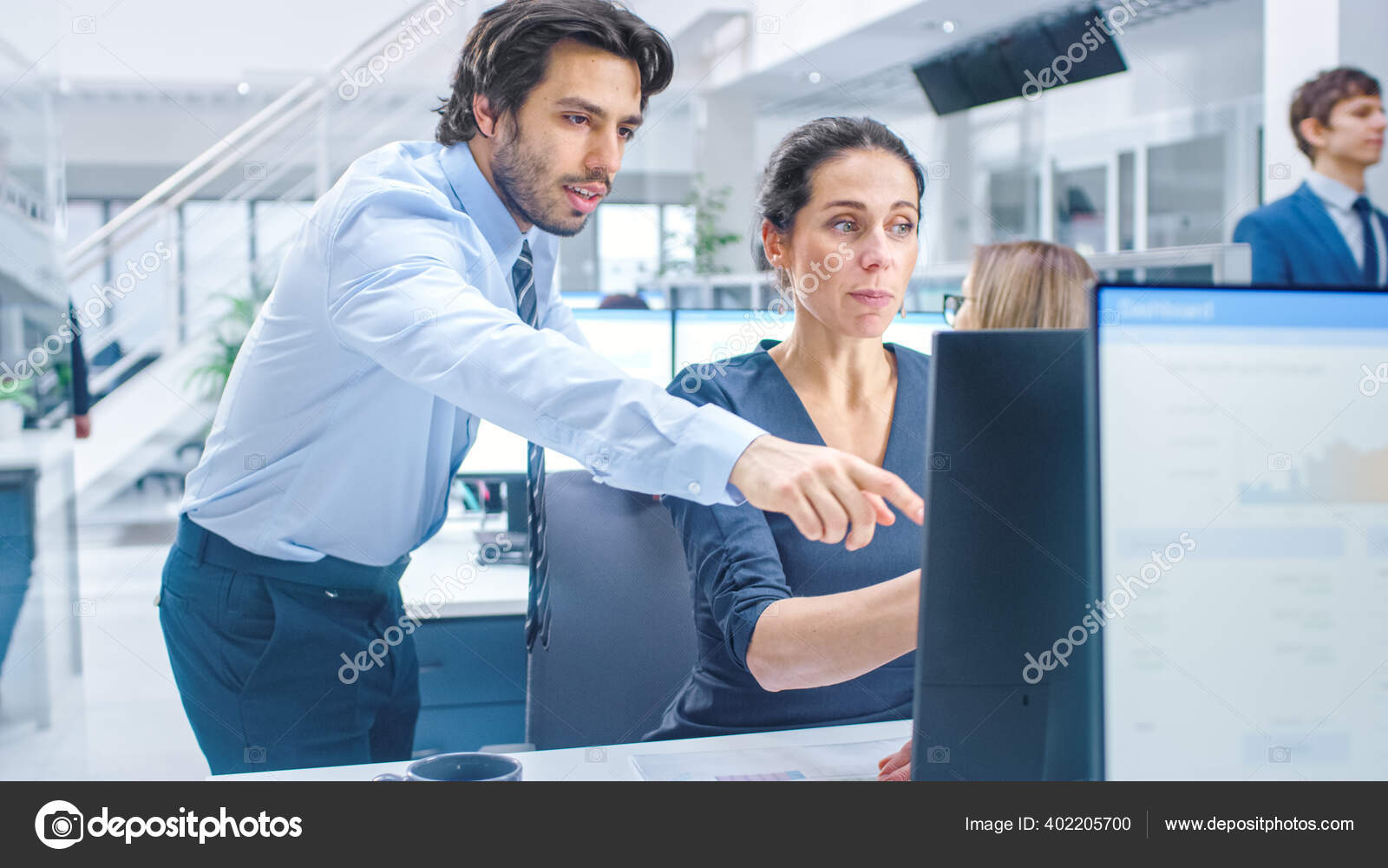 In the Busy Corporate Office: Female Manager Explains Task to Businesswoman who Works on Desktop Computer. Businesspeople an Working with Clients, Having Discussions and Analysing Statistics